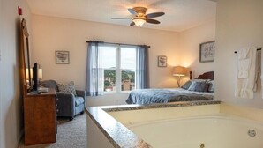 Une chambre avec une grande baignoire, un ventilateur de plafond, un bureau et une vue sur l’extérieur.