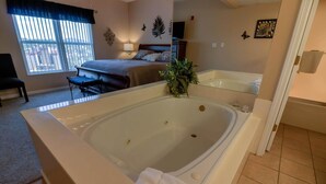 Un dormitorio amplio con una cama grande, una zona de estar con un sillón y un baño separado con bañera.