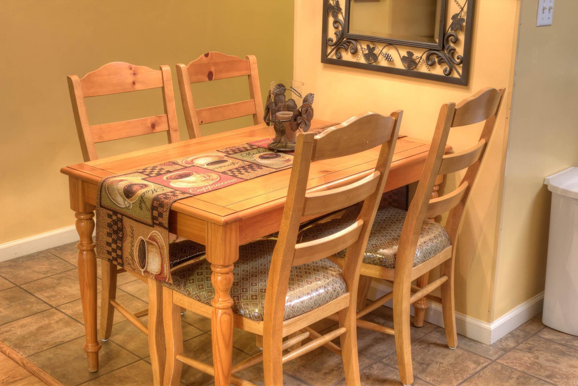 Une table à manger en bois, agrémentée d’un chemin de table à motifs, entourée de quatre chaises en bois dotées d’assises rembourrées.