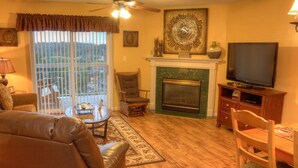 A living room with a fireplace, leather sofa, television, and a dining area with a table and chairs. - Whispering Pines 141 (Pigeon Forge)