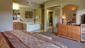 A bedroom with a large bed, a dresser, a vanity with a mirror, a bathtub, and a door leading to a bathroom. - Whispering Pines 114 (Pigeon Forge)