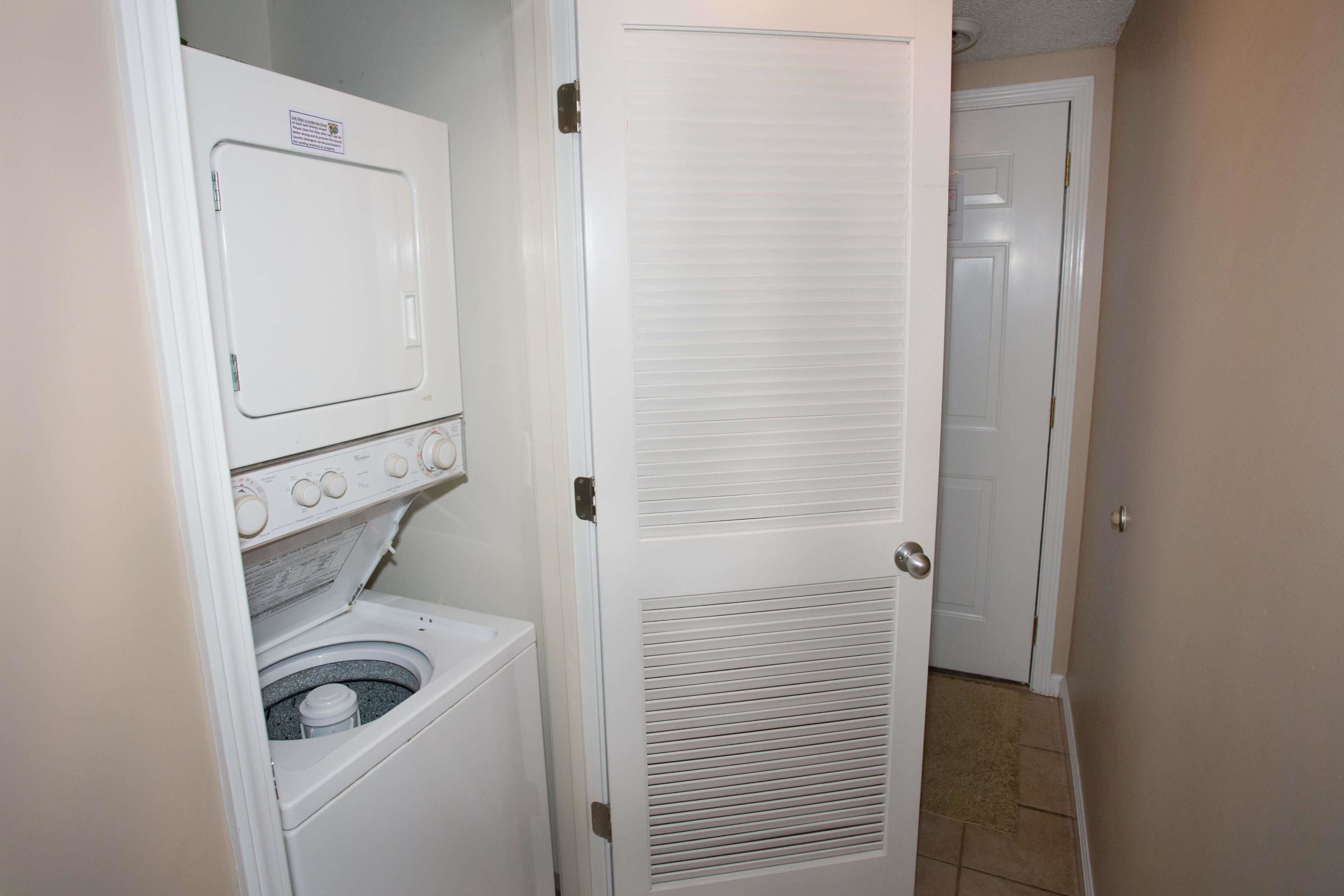 Une buanderie équipée d’un lave-linge et d’un sèche-linge à chargement frontal, d’une porte dotée d’une grille d’aération et d’un sol carrelé.