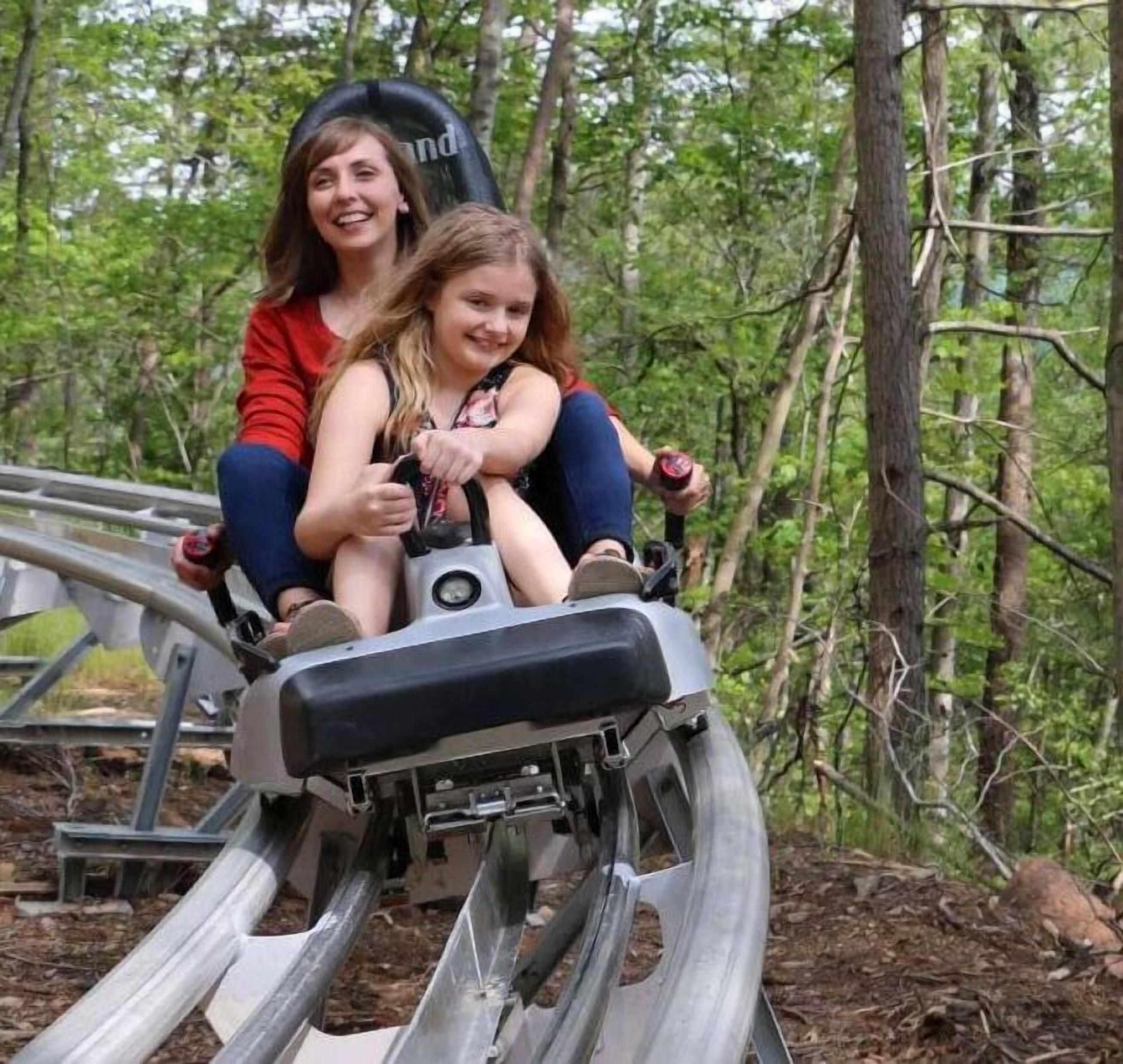 Dos personas sentadas en una vía de montaña rusa en un área boscosa.