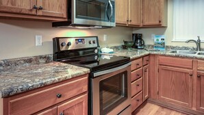 A kitchen with wooden cabinets, a stainless steel microwave, a black stove, a granite countertop, and a window with a curtain. - Whispering Pines 222 (Pigeon Forge)