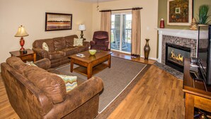 A living room with a brown leather sofa, a wooden coffee table, a fireplace, and a ceiling fan. - Whispering Pines 222 (Pigeon Forge)