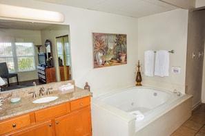 A bathroom with a large bathtub, a sink, and a mirror. There is a painting on the wall and a towel rack with towels. - Whispering Pines 104 (Pigeon Forge)