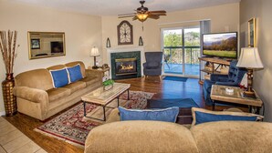 A living room with a fireplace, a ceiling fan, and a television. - Whispering Pines 104 (Pigeon Forge)