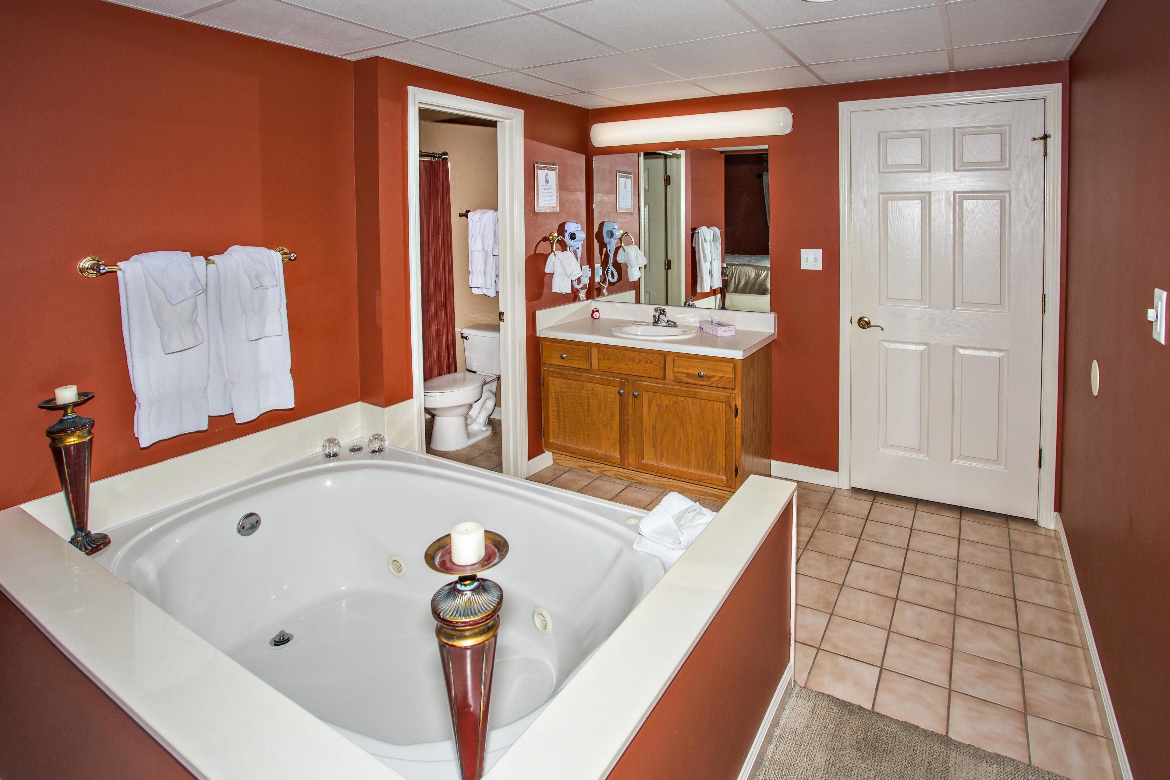 A bathroom with a large bathtub, a vanity with a mirror, and a door leading to another room.