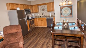 Une cuisine moderne avec des meubles en bois, des appareils électroménagers en acier inoxydable et un coin repas comprenant une table et des chaises en bois.