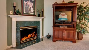 A living room with a fireplace, a television on a wooden stand, and a framed picture above the mantel. - Whispering Pines 214 (Pigeon Forge)