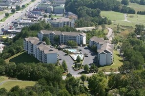A multi-story hotel with a central courtyard featuring a swimming pool, surrounded by lush greenery and parking areas. - Whispering Pines 214 (Pigeon Forge)