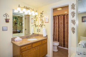 A bathroom with a wooden vanity, a large mirror, and a shower curtain. - Whispering Pines 212 (Pigeon Forge)