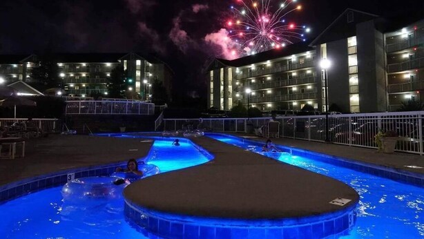 A swimming pool area with multiple pools and a large building in the background. - Whispering Pines 212 (Pigeon Forge)