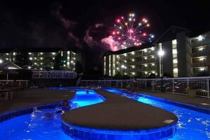 A swimming pool area with multiple pools and a large building in the background. - Whispering Pines 212 (Pigeon Forge)
