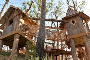 A wooden treehouse structure with a rope bridge, surrounded by trees. - Whispering Pines 212 (Pigeon Forge)