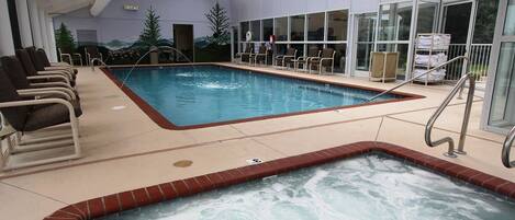 An indoor swimming pool with lounge chairs, a hot tub, and a mural on the wall.