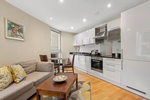 A modern kitchen with white cabinets, a dining area with a sofa and table, and a painting on the wall.