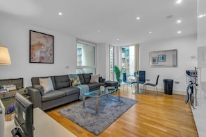 A modern living room with a grey sofa, a glass coffee table, and a large abstract painting on the wall. - Luxurious Lanterns Court Two-bedrooms Apartments (London)