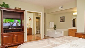 Quarto de hotel com uma cama grande, televisão, banheiro com banheira e um armário de madeira.