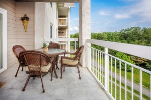 A balcony with wicker chairs and a table, overlooking a road and greenery. - Whispering Pines 242 (Pigeon Forge)