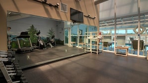 Une salle de sport équipée de matériel d’exercice, dotée d’un grand miroir et offrant une vue sur une piscine grâce à de larges fenêtres.