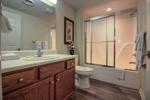 Une salle de bain avec un meuble-lavabo en bois, un lavabo blanc, des toilettes et un espace douche avec une fenêtre.