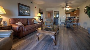 A living room with a brown leather sofa, a glass coffee table, and a dining area with metal chairs and a wooden table. - Whispering Pines 243 (Pigeon Forge)