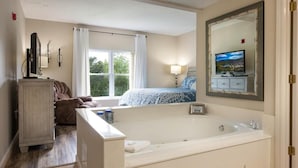 A bedroom with a large window, a bed, a TV, a mirror, and a bathtub.