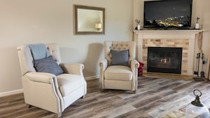 A living room with two armchairs, a fireplace, and a television mounted above it.
