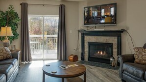 A living room with a fireplace, a television mounted above it, and a large window with curtains. - Whispering Pines 333 (Pigeon Forge)