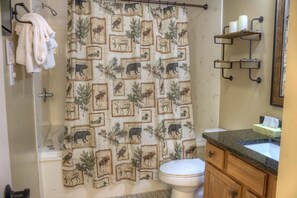 A bathroom with a shower curtain featuring wildlife prints, a toilet, a sink with a granite countertop, and a towel rack with towels. - Whispering Pines 341 (Pigeon Forge)