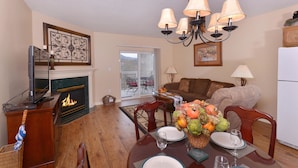 A dining area with a fireplace, chandelier, and a table set for four with plates, glasses, and a fruit centerpiece. - Whispering Pines 411 (Pigeon Forge)