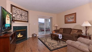 A living room with a fireplace, a television, a sofa, and a dining area with a table and chairs. - Whispering Pines 411 (Pigeon Forge)