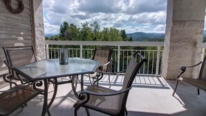 A balcony with a glass table and metal chairs, overlooking a scenic view of trees and mountains. - Whispering Pines 354 (Pigeon Forge)