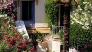 A two-story building with a balcony, a small garden with various plants and flowers, and a palm tree. - Villa Saint Hubert (Nice)