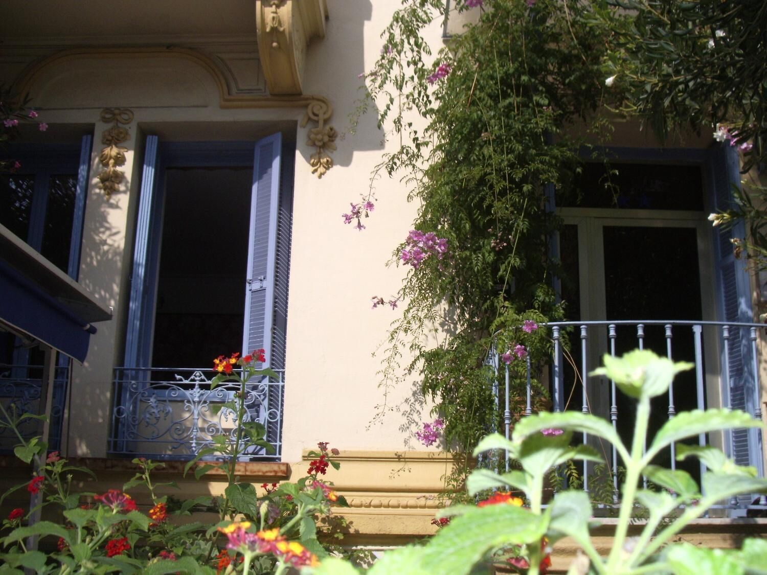 A building with a balcony, a window with shutters, and a wall with a decorative element.