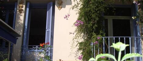 A building with a balcony, a window with shutters, and a wall with a decorative element.