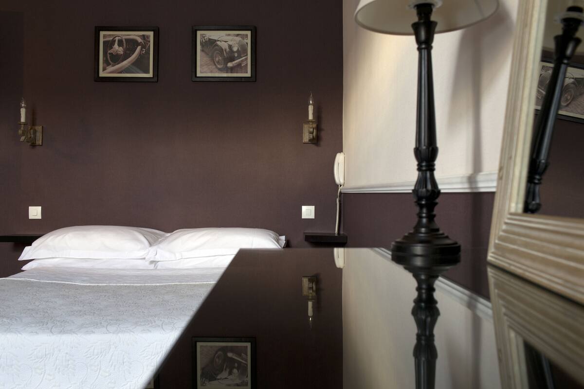 Ein Hotelzimmer mit einem Bett, einem Nachttisch, einer Lampe und zwei gerahmten Bildern an der Wand.
