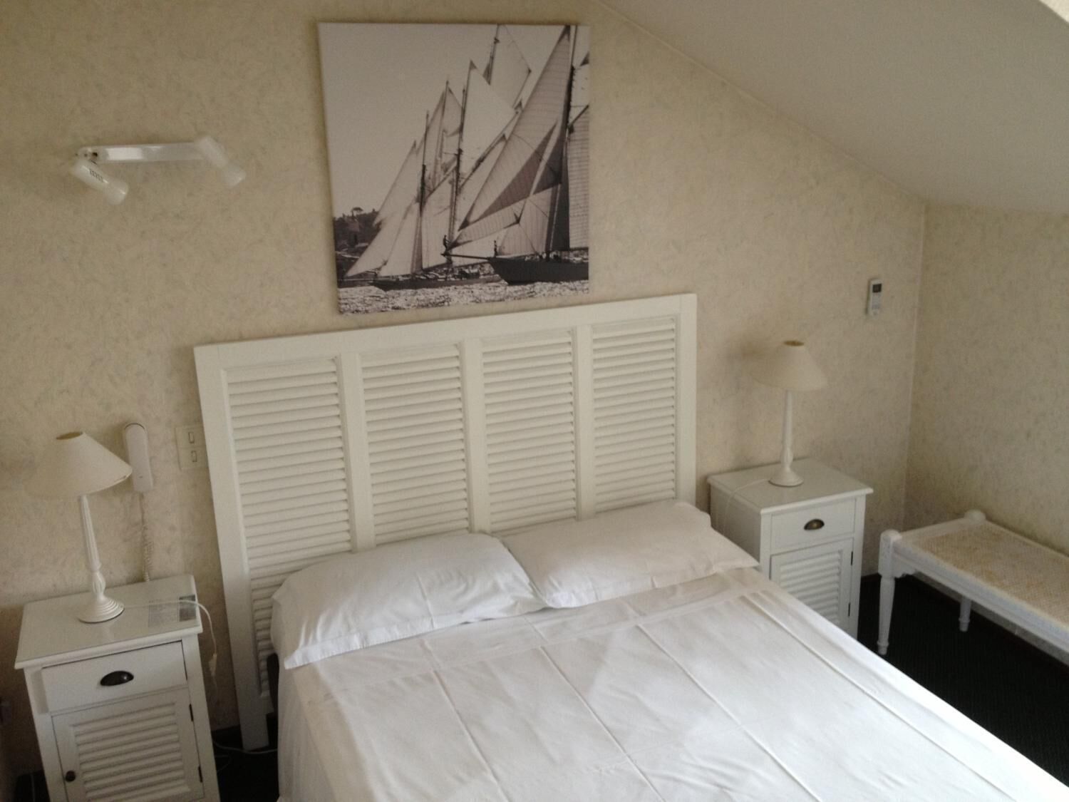 Una camera da letto con un letto, comodini bianchi, una lampada bianca e un quadro con dei velieri sulla parete.