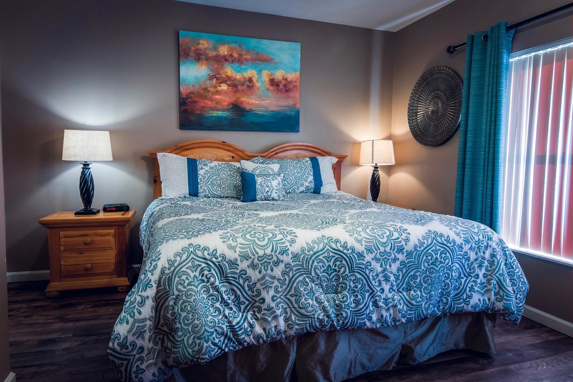 Une chambre à coucher avec un lit, deux tables de chevet, un tableau et une fenêtre avec des rideaux.