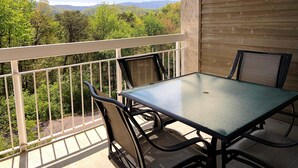 A balcony with a table and chairs, overlooking a forested area with mountains in the distance. - Whispering Pines 343 (Pigeon Forge)