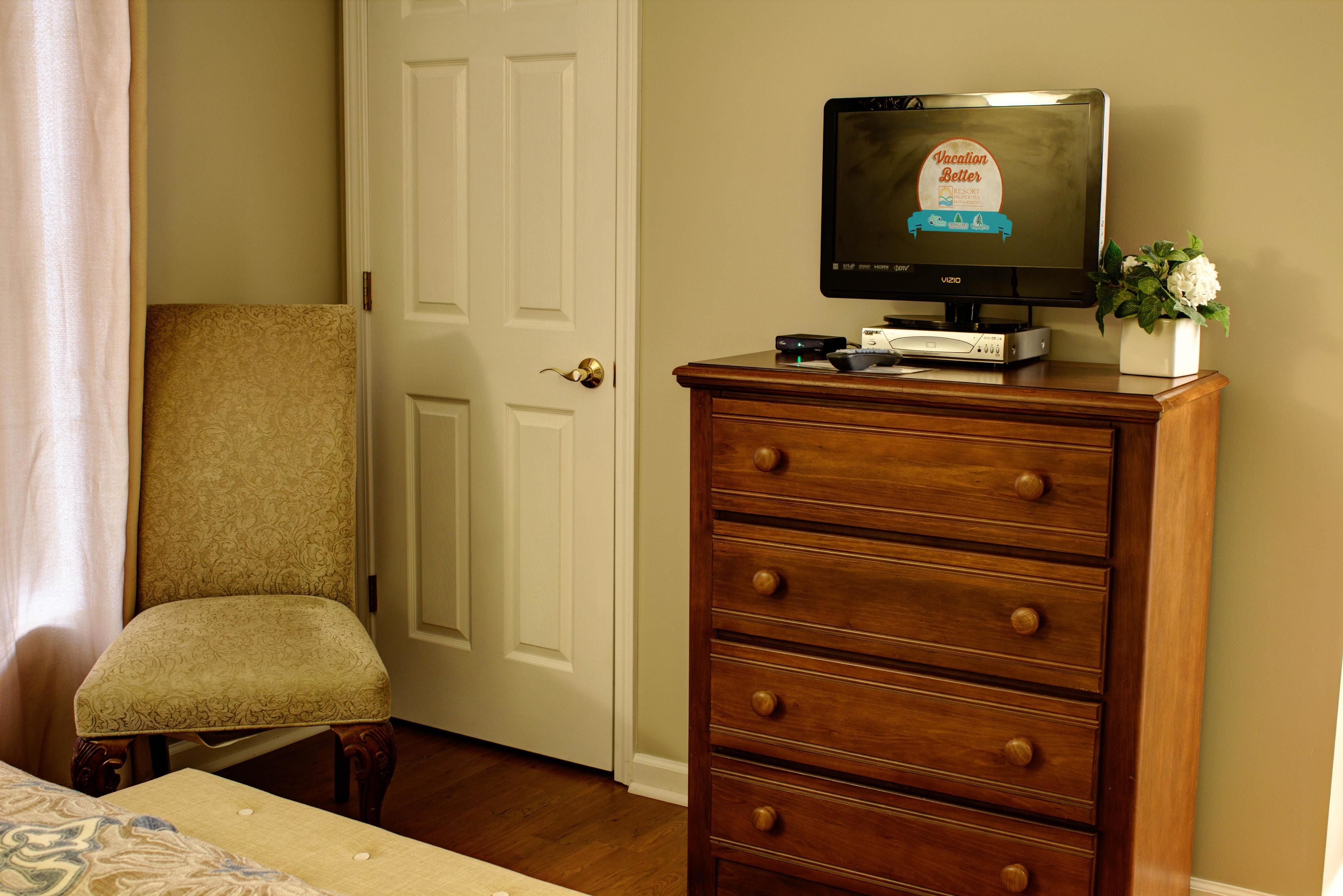 Una habitación con un aparador de madera, un televisor encima, una silla y una puerta.