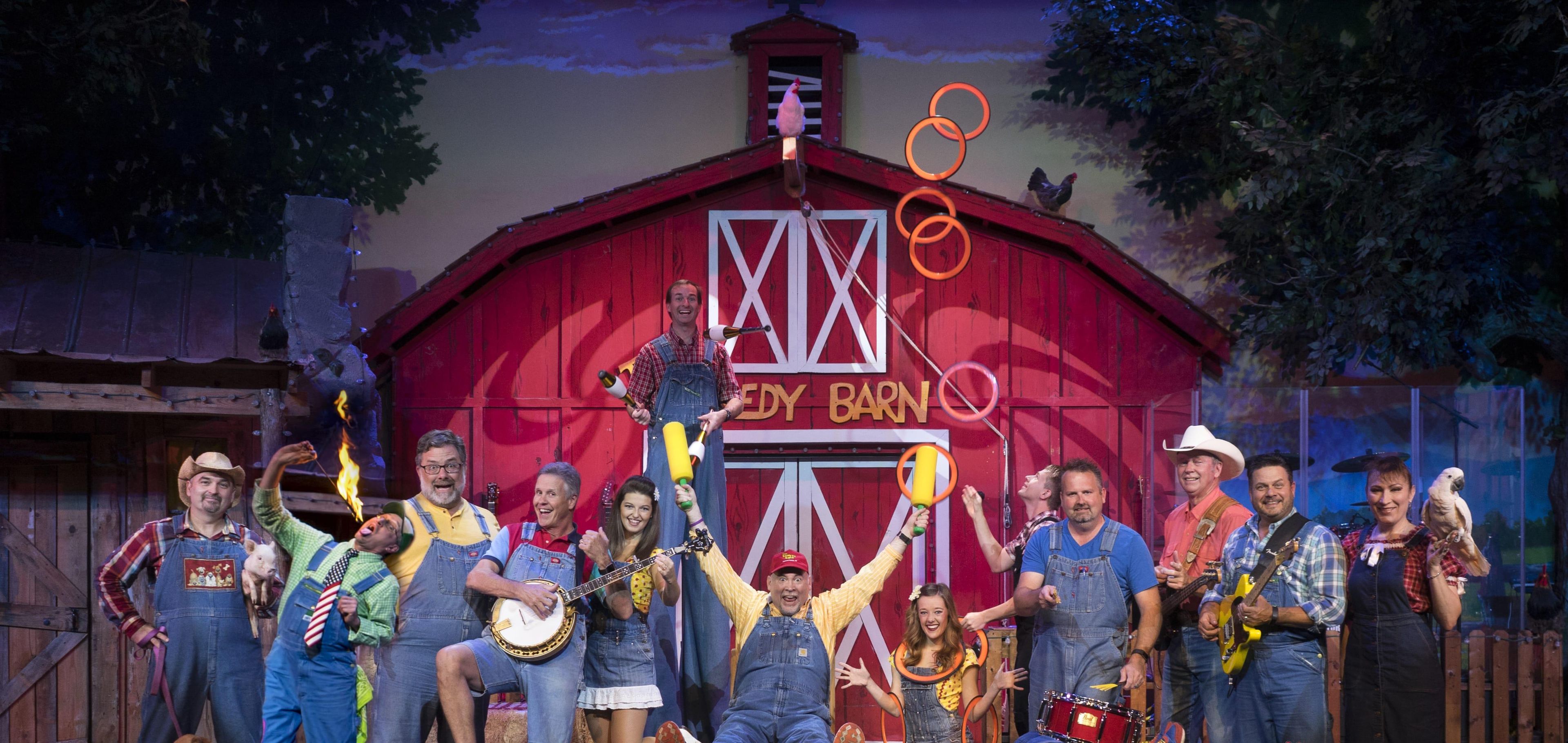 Een groep mensen voor een rode schuur met een 'EDDY BARN' bord, sommigen met muziekinstrumenten.
