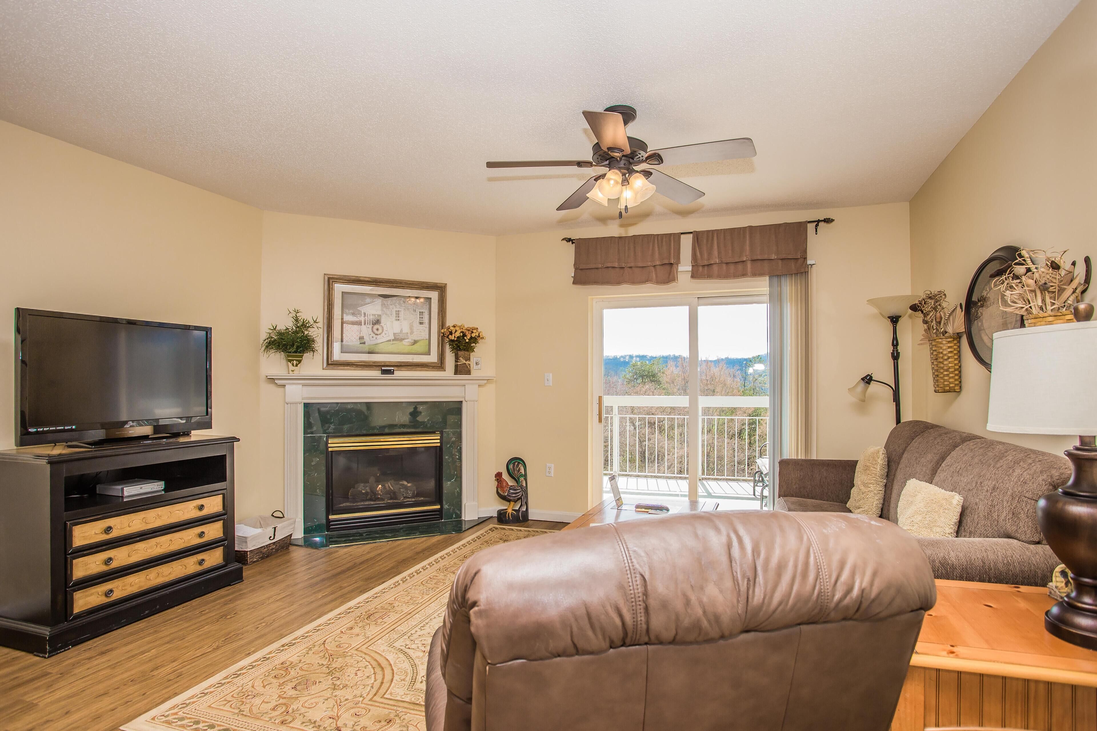 A living room with a fireplace, television, leather sofa, and a balcony with a view.