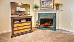 A living room with a fireplace, a television on a stand, and a framed picture above the mantel. - Whispering Pines 441 (Pigeon Forge)