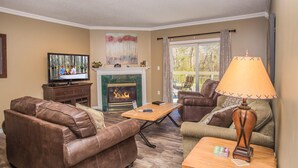 A living room with a fireplace, leather sofas, a coffee table, and a television. - Whispering Pines 413hc (Pigeon Forge)