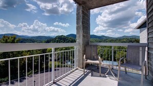 Een balkon met uitzicht op bergen, een stenen pilaar en buitenmeubilair.