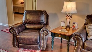 A leather armchair with a wooden table and a lamp in a room with wooden flooring and a red rug. - Whispering Pines 444 (Pigeon Forge)