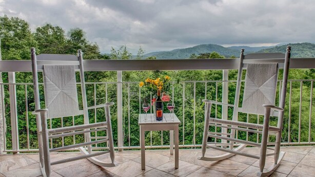 A balcony with two rocking chairs, a small table, and a vase with flowers. - Whispering Pines 444 (Pigeon Forge)