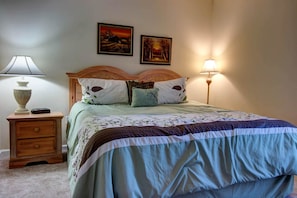 A bedroom with a bed, two bedside lamps, a nightstand, and two framed pictures on the wall.